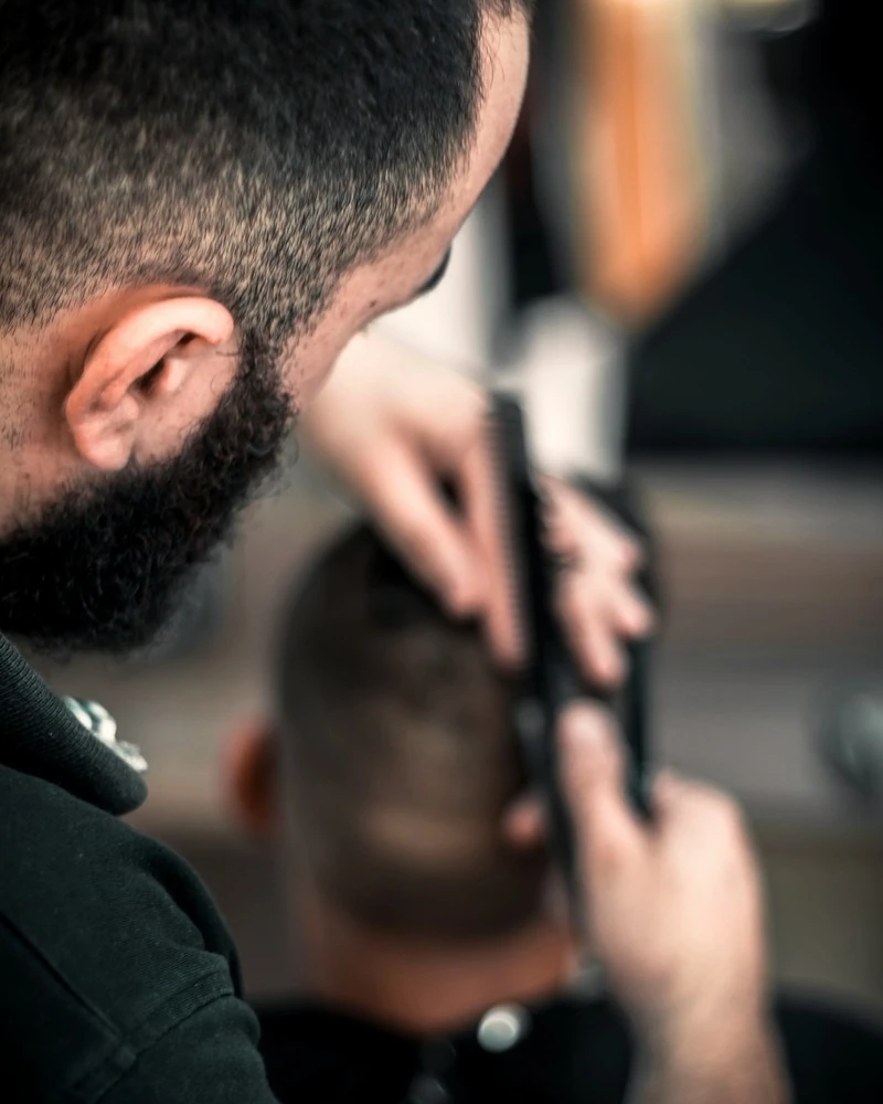 Barber menyisir dan merapikan rambut pelanggan, terlihat dari balik bahunya