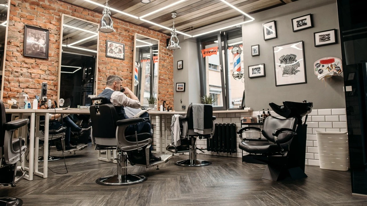 Een barbershop met bakstenen muren, hoge spiegels en lege stoelen, een barbier leest aan de balie