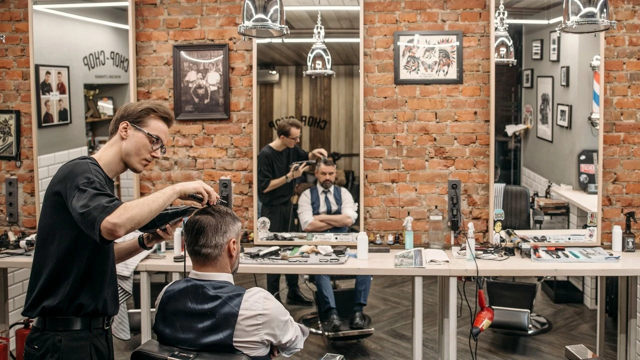 Um barbeiro corta o cabelo de um cliente em uma barbearia clara com paredes de tijolo e espelhos